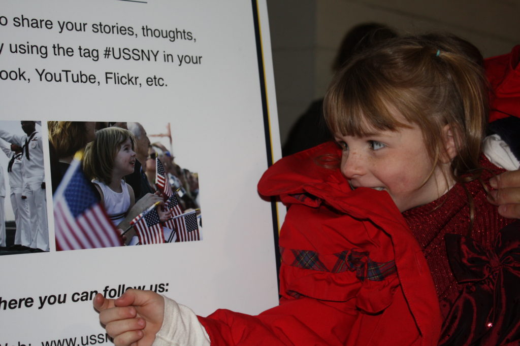 Little girl in red coat looking at picture of little girl with a lot of American Flags