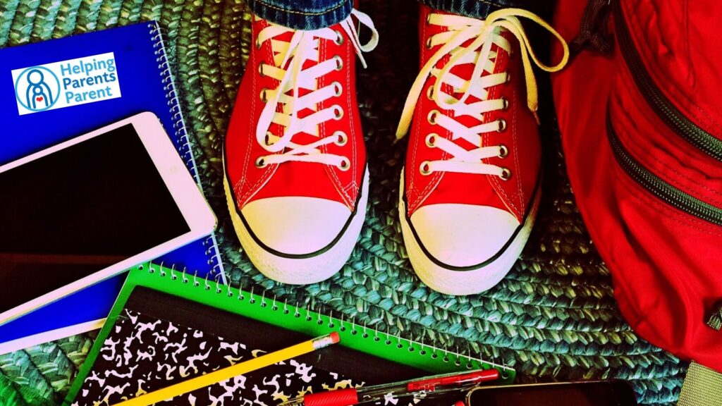 Looking down at red sneakers and a mess of notebooks, writing utensils, a calculator and a backpack.